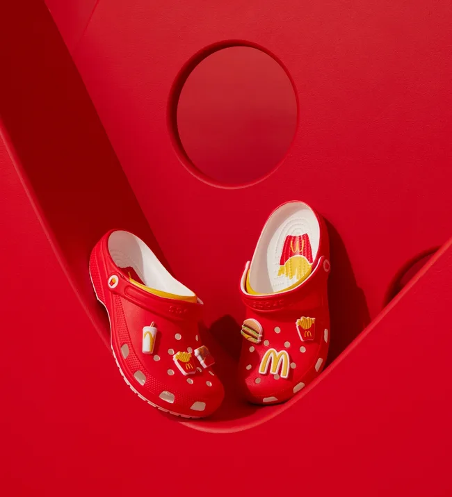 Red Crocs decorated with McDonald's food charms against a matching red background.