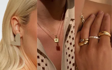 Heart-shaped earring, gold necklace with a square pendant, and a hand with three gold rings.
