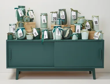 Decorative advent calendar jars with numbered tags on a green cabinet.