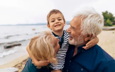 Three people smiling, with a child hugging two adults on a beach.
