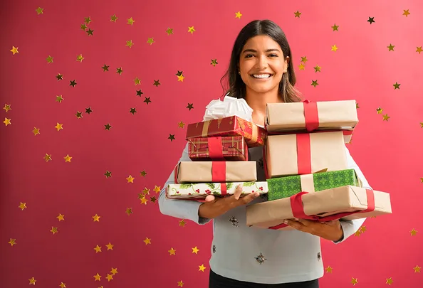 Smiling person holding stacked gift boxes with red ribbons on a starry red background.