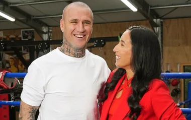 A man with tattoos and a woman in a boxing gym, smiling at each other.