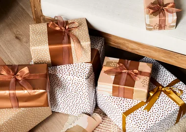 Gift boxes wrapped in brown and white patterned paper with bows, placed on a wooden floor by a white bench.