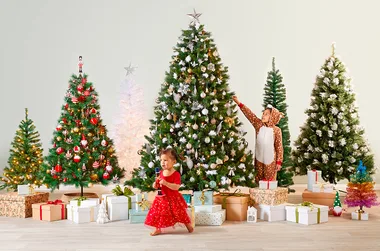 Children around decorated Christmas trees with gifts underneath. A child in a reindeer onesie and another in a red dress.