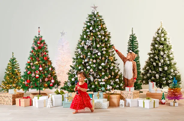 Children around decorated Christmas trees with gifts underneath. A child in a reindeer onesie and another in a red dress.
