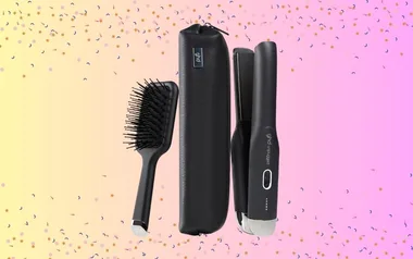 GHD Unplugged hair straightener, brush, and case on a pink and yellow confetti background.