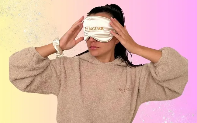 Person wearing a beige robe and an eye mask labeled "ByJAGUAR" against a pastel background.
