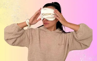 Person wearing a beige robe and an eye mask labeled "ByJAGUAR" against a pastel background.