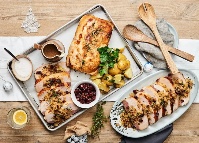 Roasted turkey breast with potatoes, gravy, and cranberry sauce on a table with wooden utensils.