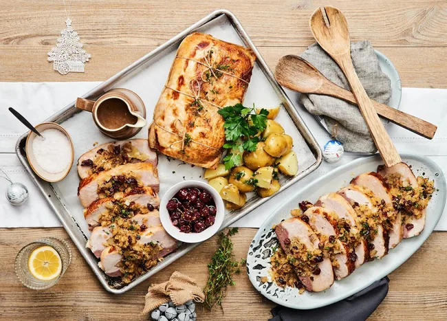 Roasted turkey breast with potatoes, gravy, and cranberry sauce on a table with wooden utensils.