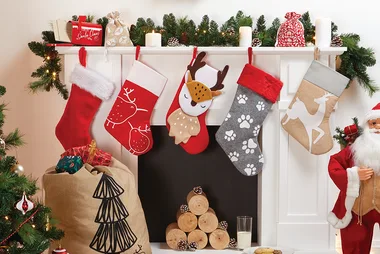 Christmas stockings hanging on a mantel with festive decorations and a Santa Claus figure nearby.