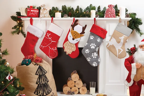 Christmas stockings hanging on a mantel with festive decorations and a Santa Claus figure nearby.