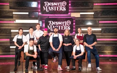 Group of chefs posing in front of "Dessert Masters" sign, wearing aprons, smiling for the camera.