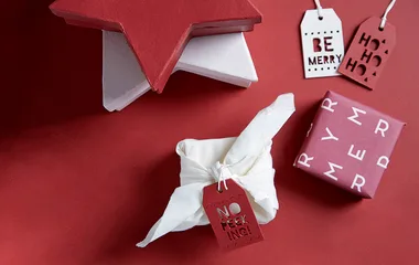 Gift boxes and tags on a red background, one with "No peeking!" tag, festive star box, and "Be Merry" tag.
