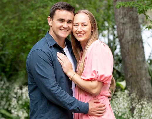A couple smiling and embracing in a lush green outdoor setting.