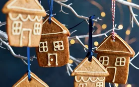 Gingerbread cookies shaped like houses, decorated with white icing, hanging on a white branch with colorful ribbons.