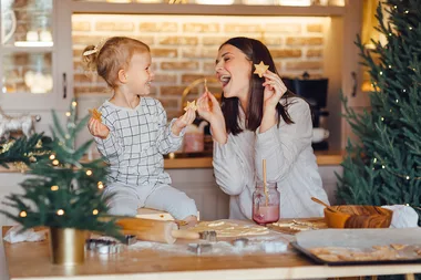 Mother and child joyfully baking star-shaped cookies in a kitchen decorated for Christmas.