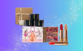 Gift set with candles, skincare boxes, illustrated card, and red and nude lipsticks on a blue gradient background.