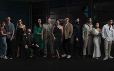 Group of 12 people pose in stylish attire, standing in front of a glass building entrance.