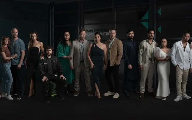 Group of 12 people pose in stylish attire, standing in front of a glass building entrance.