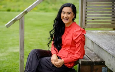 Woman in a red blouse smiles while sitting on outdoor wooden steps, with green grass in the background.