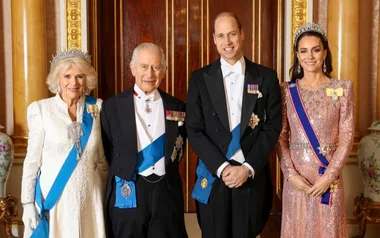 A royal group in elegant attire with sashes and tiaras, standing in a formal setting.