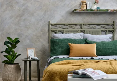Cozy bedroom with green bed, mustard throw, striped pillows, and a plant on a side table next to wall art and decor shelf.
