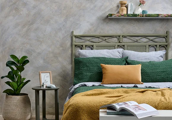 Cozy bedroom with green bed, mustard throw, striped pillows, and a plant on a side table next to wall art and decor shelf.
