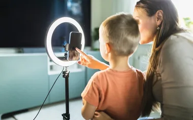 Woman and child using a smartphone on a tripod with a ring light in a home setting.