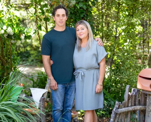 Couple standing in a lush green garden, smiling and posing for a photo.
