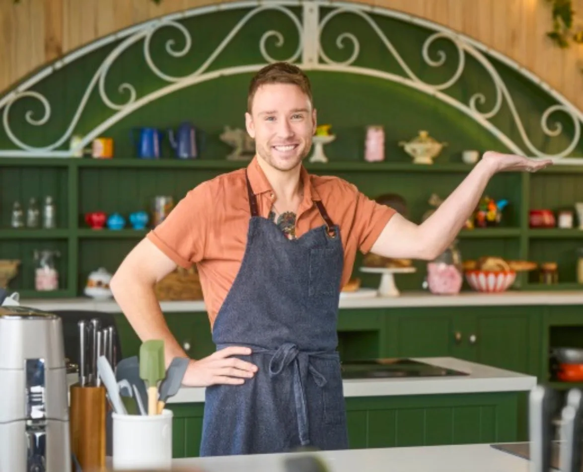 Man in apron cheerfully presenting in a decorative kitchen.