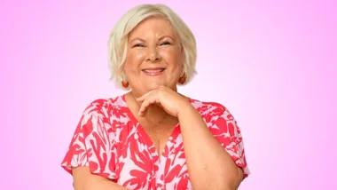 A woman with short blonde hair, smiling in a pink floral top against a pink background.