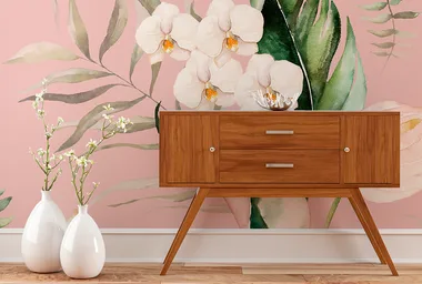 Mid-century modern wooden console against pink floral wallpaper with two white vases holding flowers.
