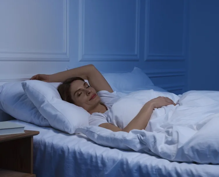 Woman sleeping peacefully in bed with white bedding and soft lighting.