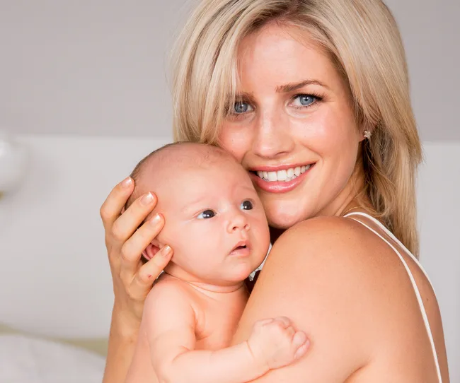A woman smiling while holding a baby close in her arms.