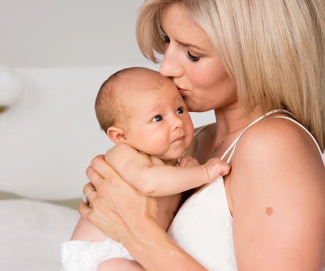 A woman lovingly kisses a baby on the head in a tender embrace.