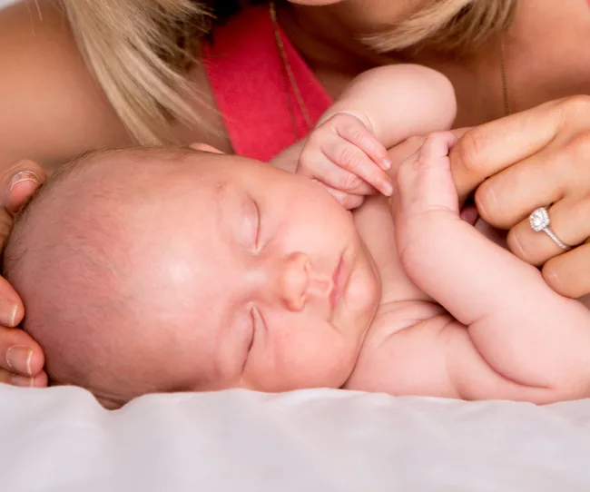 Sleeping baby held by a woman with a diamond ring, lying on a soft white surface.