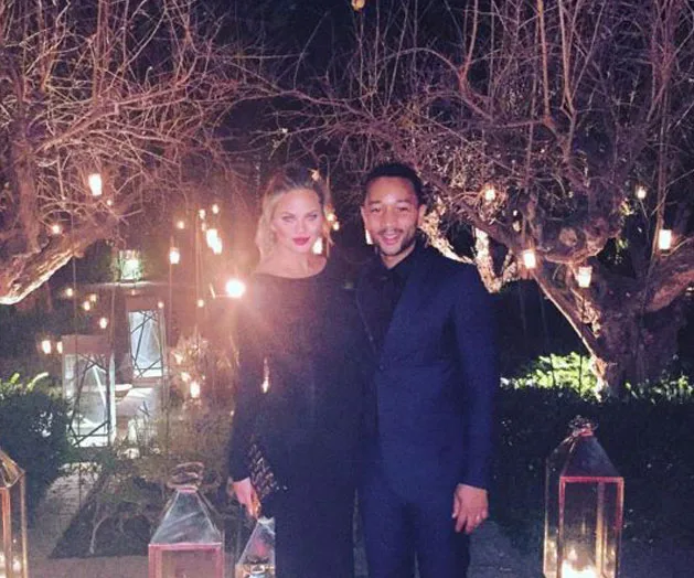 Couple posing together outdoors at night with string lights and lanterns, dressed in formal black attire.