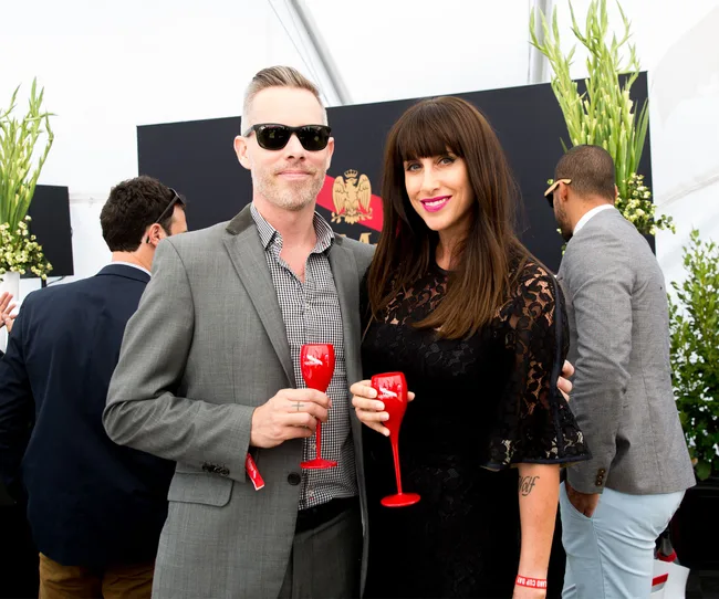 A man and woman holding red glasses, dressed formally, standing together at a social event.