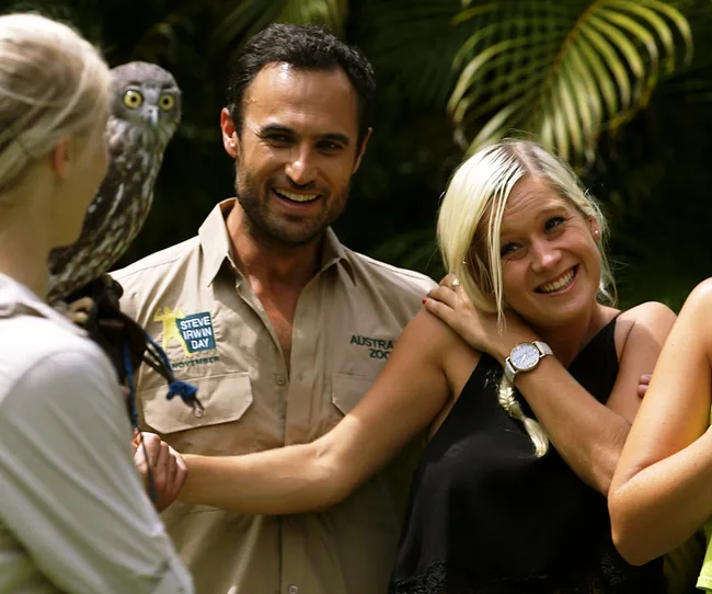 Group of people smiling with an owl at Australia Zoo, one wearing "Steve Irwin Day" shirt.