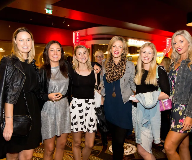 Group of six women smiling and posing together in a lively indoor setting with vibrant red lighting.