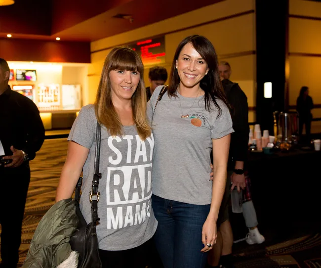 Two women smiling and posing indoors; one wears a "Stay Rad Mama" shirt, the other a "Life's a Peach" shirt.