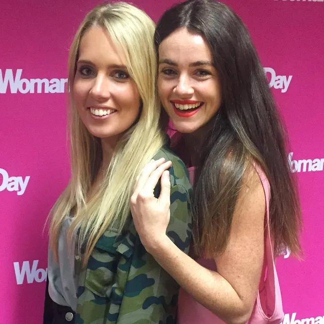 Two women smiling in front of a pink "Woman's Day" backdrop.