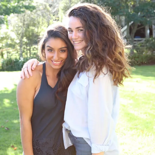 Two women smiling and embracing in a sunny garden setting.