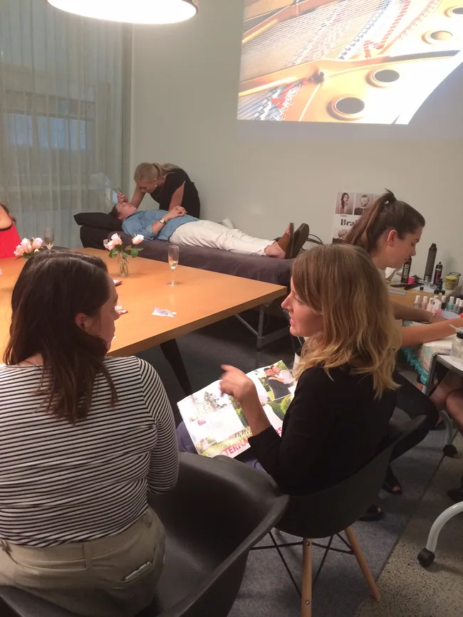 Women receiving beauty treatments and reading magazines in a room with a projected image on the wall.