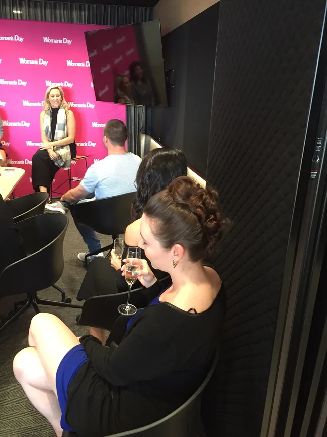 A group of people sitting in a room, one woman in the foreground holding a drink.