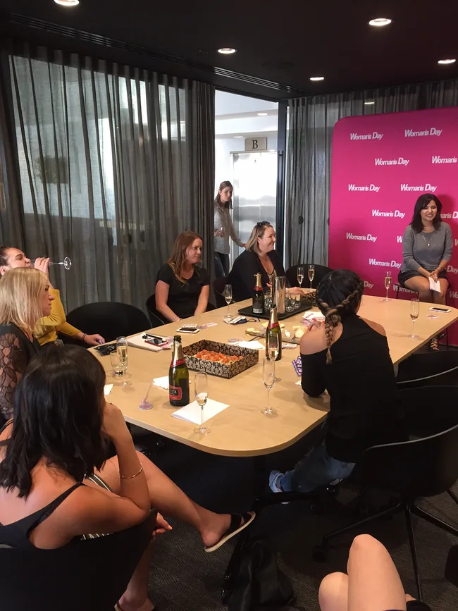 A group of women sitting around a table with drinks at a Woman's Day event in a conference room.