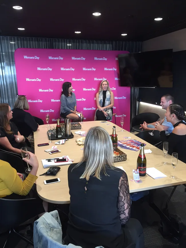 Group discussion around a table in a Women's Day meeting room, with two speakers in front of a pink backdrop.