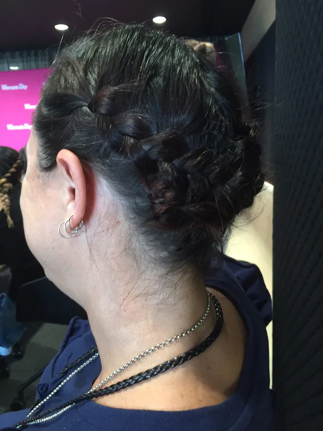 Woman with braided hairstyle, wearing hoop earrings and layered necklaces, facing away.