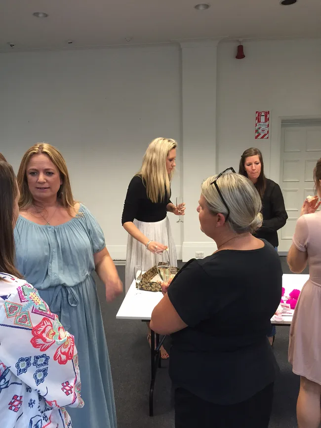 Group of women in casual attire conversing around a table with drinks in a room.